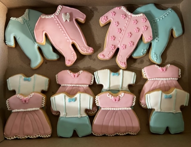 Baby shower cookies shaped as onesies and dresses in pink and blue