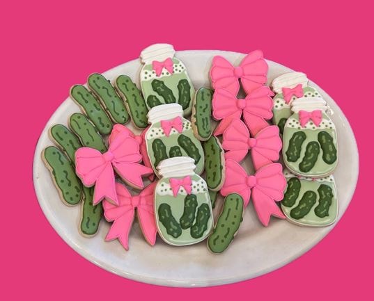 Pickle jar and pickle cookies with pink bows on a white plate against pink background