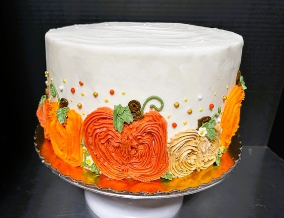 Fall autumn themed cake with orange pumpkin and floral frosting decorations on white base