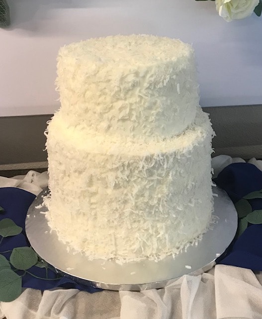 Two-tier coconut cake covered in shredded coconut frosting on silver board